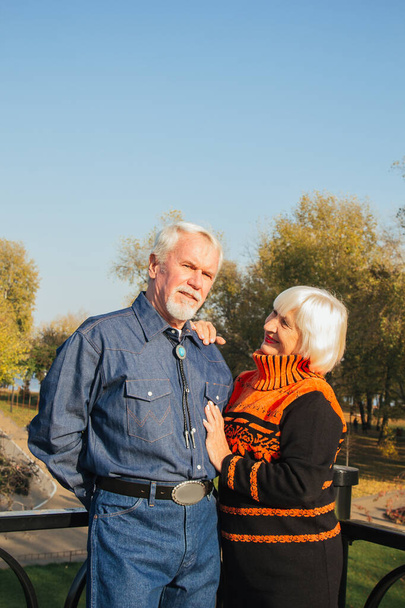 Happy elderly man and woman sitting on a bench in autumn day. Relaxed senior couple sitting on a park bench. Grandfather gently kisses grandmother on the forehead. - Valokuva, kuva