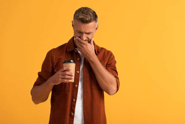 sad man covering face while looking at paper cup isolated on orange  - 写真・画像