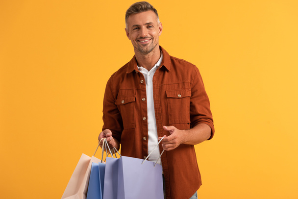 happy man holding shopping bags isolated on orange  - Fotoğraf, Görsel