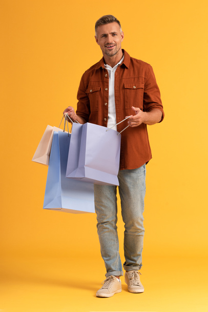 happy man holding shopping bags while standing on orange  - Photo, Image