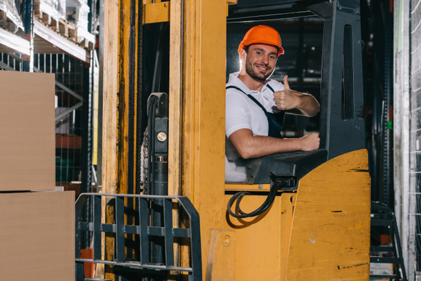 smiling warehouse worker showing thumb up and looking at camera while operating forklift loader - Photo, Image