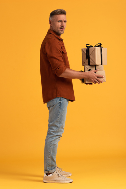 удивленный мужчина держит в руках подарки, стоя на апельсине
  - Фото, изображение