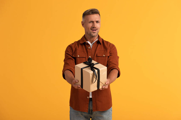 emotional man holding present isolated on orange  - Zdjęcie, obraz