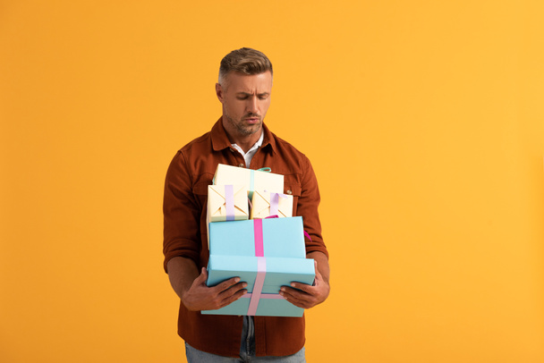 handsome man looking at gift boxes isolated on orange  - Foto, Bild