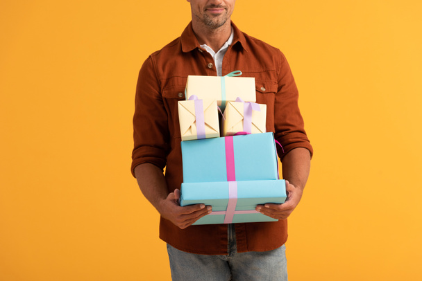 vista recortada del hombre sonriendo mientras sostiene cajas de regalo aisladas en naranja
  - Foto, imagen