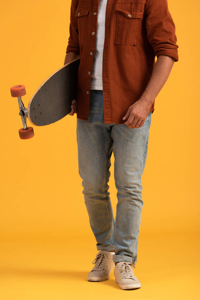 cropped view of man holding penny board on orange  - Фото, изображение