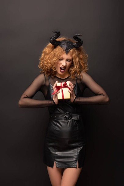 страшная кудрявая женщина в малефисентском костюме держит подарочную коробку на Хэллоуин на черном
  - Фото, изображение