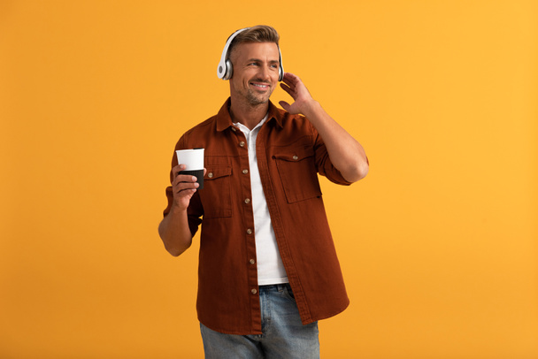 happy man listening music and holding coffee to go isolated on orange  - Fotografie, Obrázek