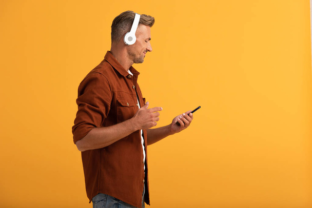 happy man listening music and holding smartphone isolated on orange  - Fotoğraf, Görsel
