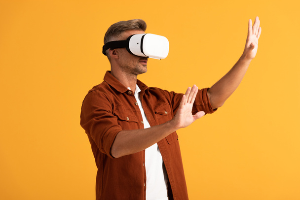 handsome man in virtual reality headset gesturing isolated on orange  - Foto, imagen