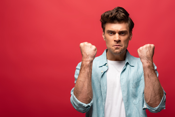 portrait of angry man in casual clothes showing fists isolated on red - Foto, immagini