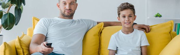 panoráma lövés jóképű apa és boldog fiú néz TV-t otthon  - Fotó, kép