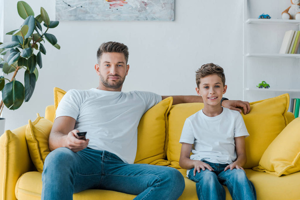 knappe vader en gelukkig zoon kijken tv thuis  - Foto, afbeelding