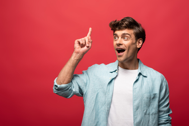 portrait of surprised man in casual clothes pointing up and having idea, isolated on red - Foto, Imagem