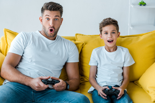 KYIV, UKRAINE - OCTOBER 2, 2019: surprised father and son playing video game at home  - Fotografie, Obrázek