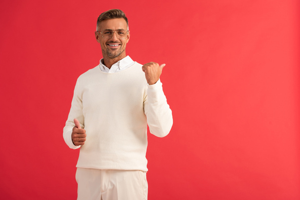 stylish and cheerful man in glasses showing thumbs up isolated on red  - Foto, imagen