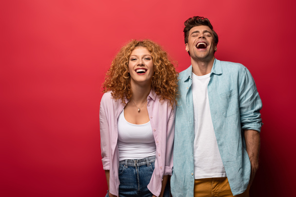 beautiful happy couple in casual clothes laughing isolated on red - Foto, imagen