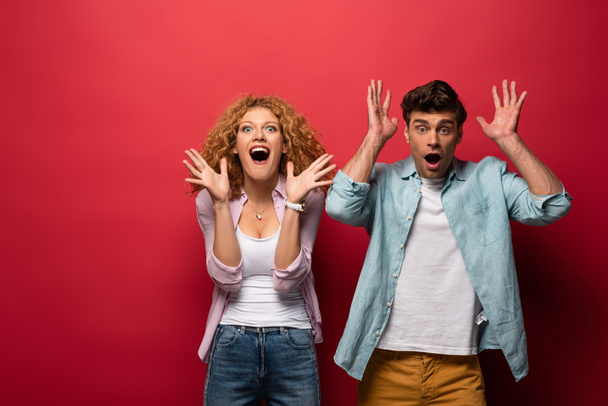 excited woman and shocked man gesturing in casual clothes isolated on red - Foto, afbeelding