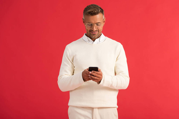 happy man in glasses using smartphone isolated on red  - Фото, зображення