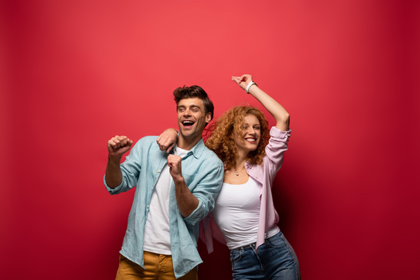 beautiful excited couple dancing in casual clothes isolated on red - Foto, Imagem