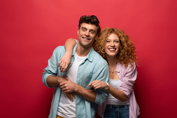 portrait of smiling couple in casual clothes isolated on red - Фото, зображення
