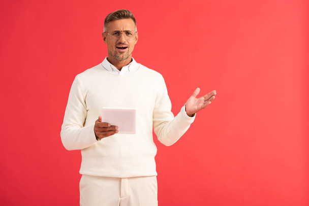shocked man gesturing while holding digital tablet isolated on red  - Foto, Imagem