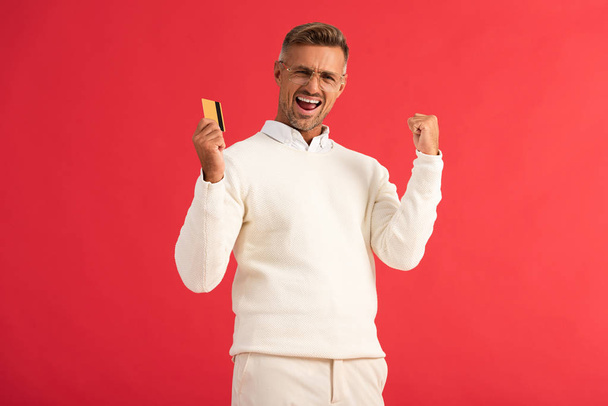 excited man in glasses holding credit card isolated on red  - Zdjęcie, obraz