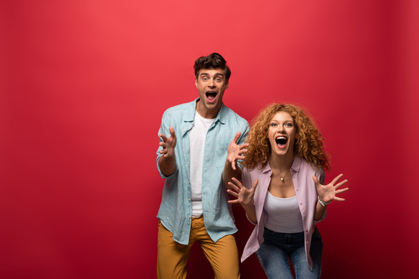 beautiful shocked couple screaming and gesturing, isolated on red - Foto, Imagen