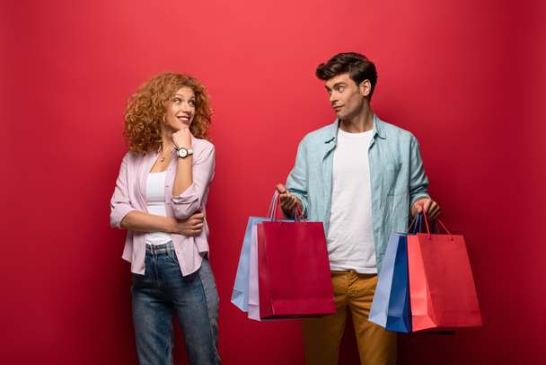 beautiful smiling couple holding shopping bags, isolated on red - Foto, Imagem