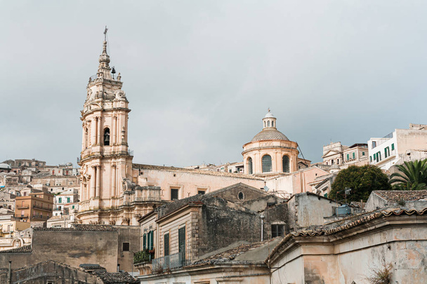 MODICA, ITALY - OCTOBER 3, 2019: baroque cathedral of san giorgio near houses against sky with clouds in sicily  - Foto, imagen