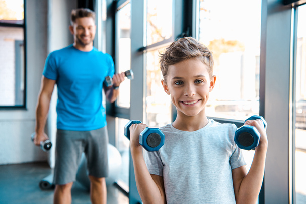 selective focus cute kid exercising with dumbbells near father  - Photo, Image