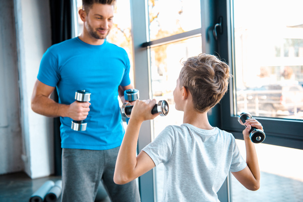enfoque selectivo niño haciendo ejercicio con pesas cerca de padre guapo
  - Foto, Imagen