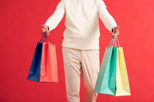 cropped view of man holding colourful shopping bags isolated on red  - Fotoğraf, Görsel