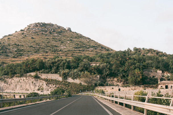 asphalt road near green trees on hill in ragusa, italy  - Фото, зображення