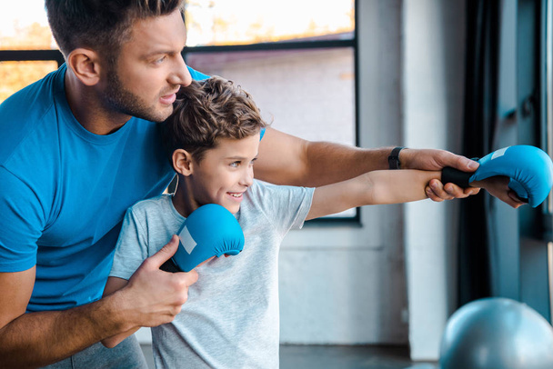 father touching hands of cute son in boxing gloves exercising in gym  - Zdjęcie, obraz