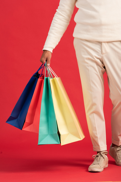 oříznutý pohled na muže držícího barevné nákupní tašky izolované na červené  - Fotografie, Obrázek