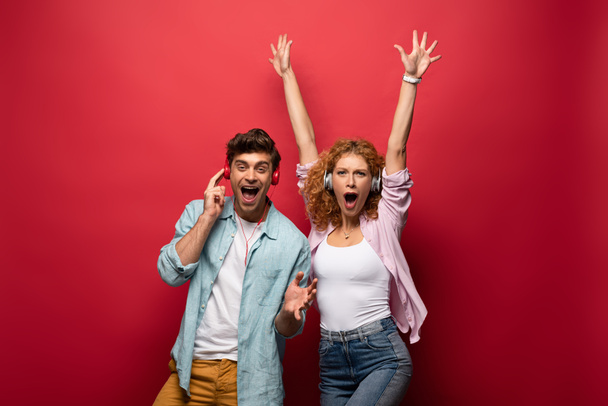 excited couple listening music with headphones together, isolated on red - Foto, Bild