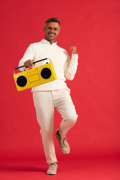 positive man in glasses holding yellow boombox on red  - Φωτογραφία, εικόνα