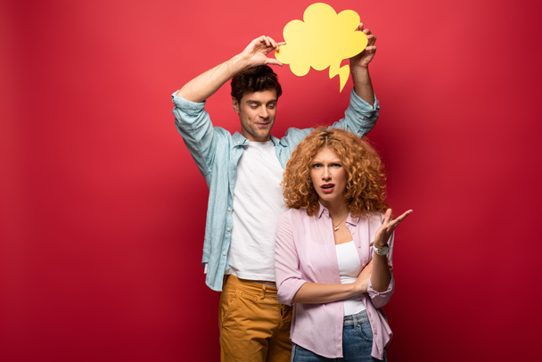 boyfriend holding yellow cloud bubble over quarreling girlfriend, on red - Foto, afbeelding