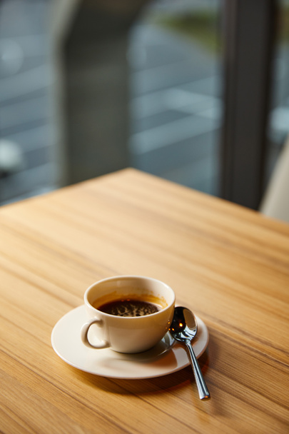 selectieve focus van kopje met koffie in de buurt lepel op houten tafel in cafe  - Foto, afbeelding