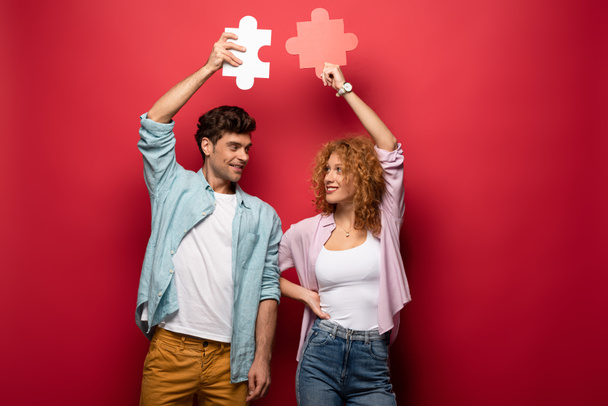 happy couple holding puzzle pieces, isolated on red - Fotoğraf, Görsel