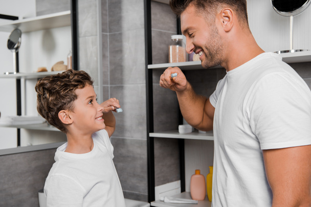 bambino felice tenendo lo spazzolino da denti e guardando il padre in bagno
  - Foto, immagini