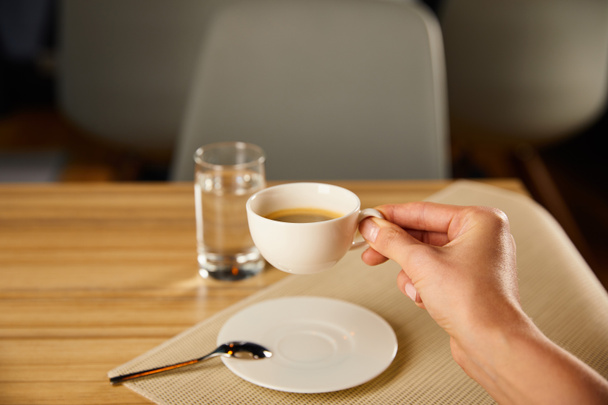 cropped view of woman holding cup of coffee near glass of water in cafe  - Photo, Image