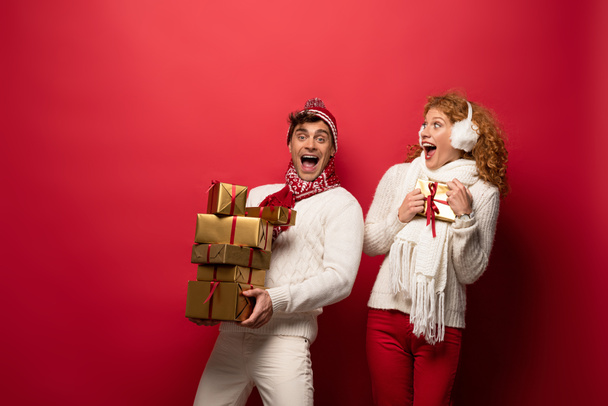excited couple in winter outfit holding christmas presents on red - Photo, Image
