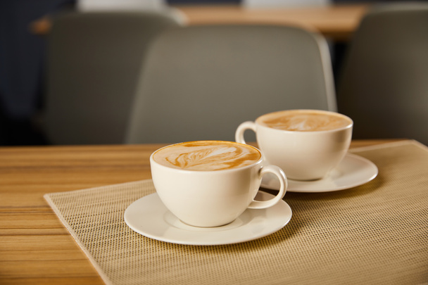 selective focus of creamy cappuccino in white cups on table  - Foto, Bild