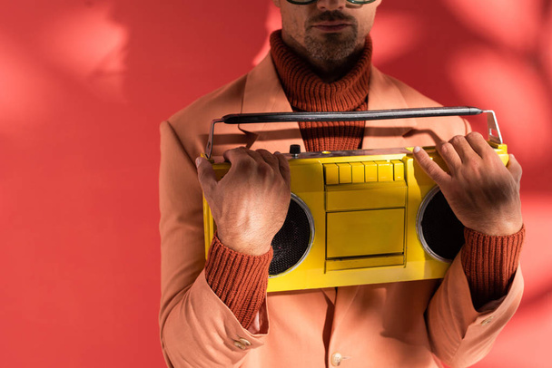 cropped view of stylish man holding yellow boombox on red with shadows  - Φωτογραφία, εικόνα
