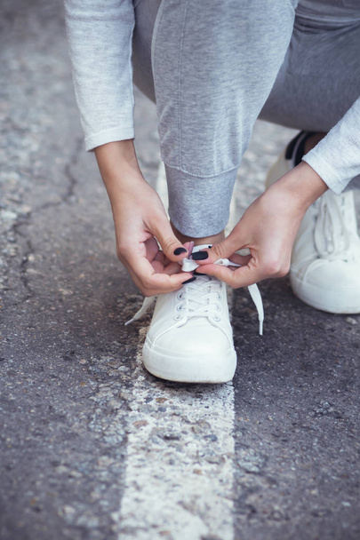 girl squatted down to tie shoelaces on white sneakers on asphalt road, autumn sport concept outdoors - Foto, Imagem