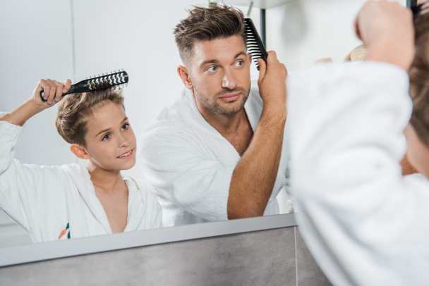 valikoiva painopiste komea mies ja söpö lapsi harjaus hiukset kylpyhuoneessa
  - Valokuva, kuva
