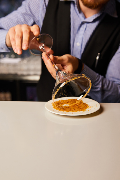 bijgesneden weergave van een bebaarde barman met margarita glas in de buurt van schotel met bruine suiker  - Foto, afbeelding