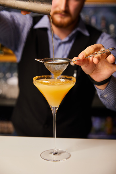 vista ritagliata del cocktail barista versando mentre tenendo shaker vicino setaccio e vetro margarita
  - Foto, immagini